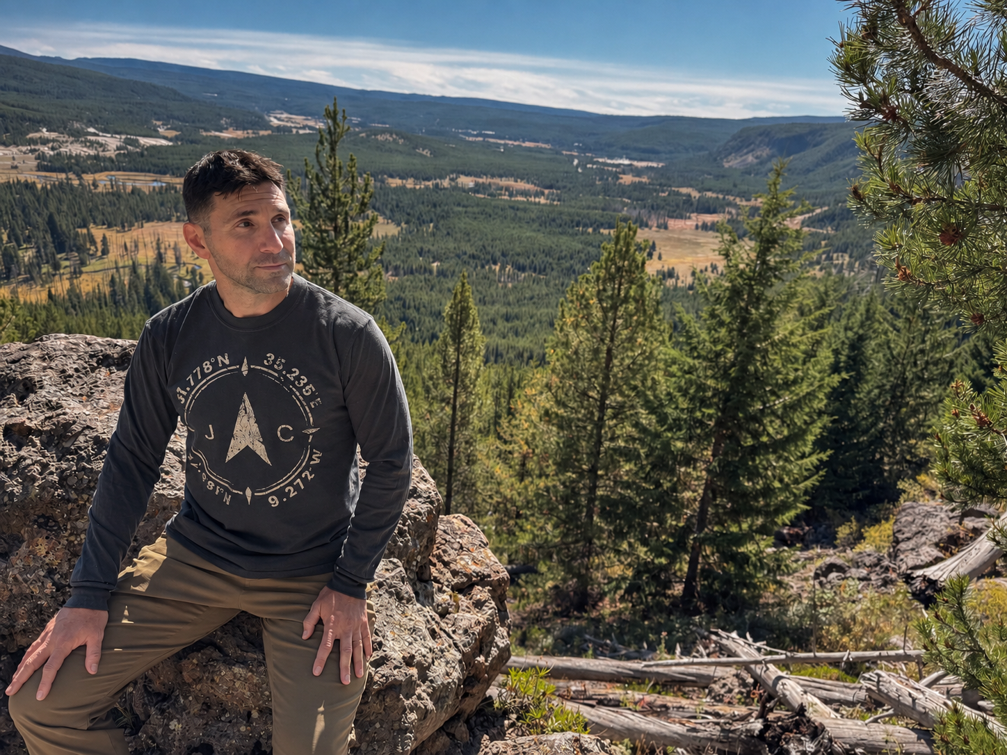Man wearing the Compass long-sleeve seated on rocks above a forested valley